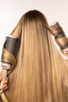 A person with long, straight blonde hair being styled with two BHBD round hairbrushes, showcasing a smooth and voluminous hair finish.