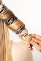 Close-up of a BHBD round brush styling blonde hair, showcasing its ceramic and ionic design for smooth, shiny, and voluminous results.