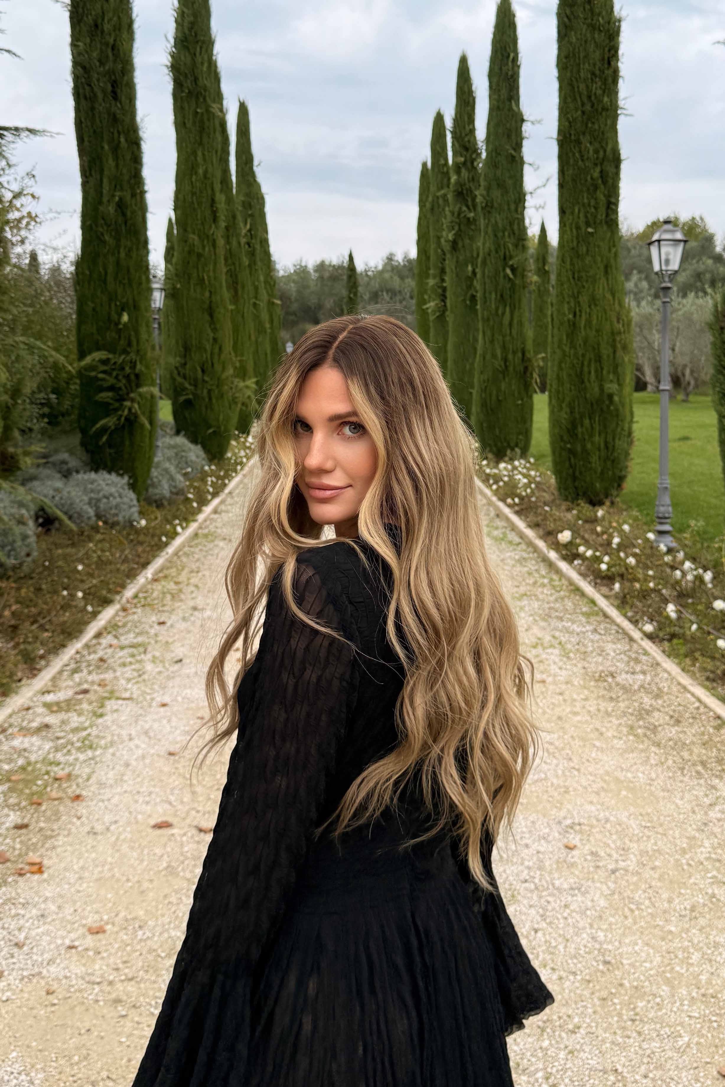 Woman wearing a long BHBD wig with dark blonde roots that transitions into slightly lighter lengths.