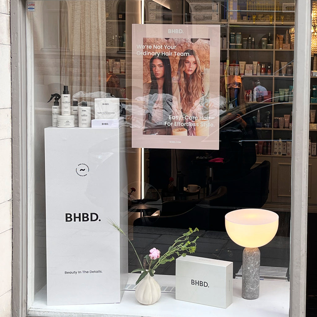 View of a salon window showcasing BHBD hair care products and marketing materials. 